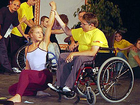 Chłopak na wózku inwalidzkim podnosi ręke dziewczynki kucającej obok niego